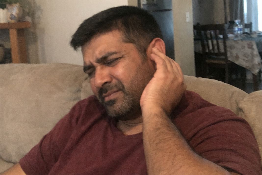 a photo of a man sitting at home rubbing or adjusting their ear while looking slightly uncomfortable a photo of a man sitting at home rubbing or adjusting their ear while looking slightly uncomfortable